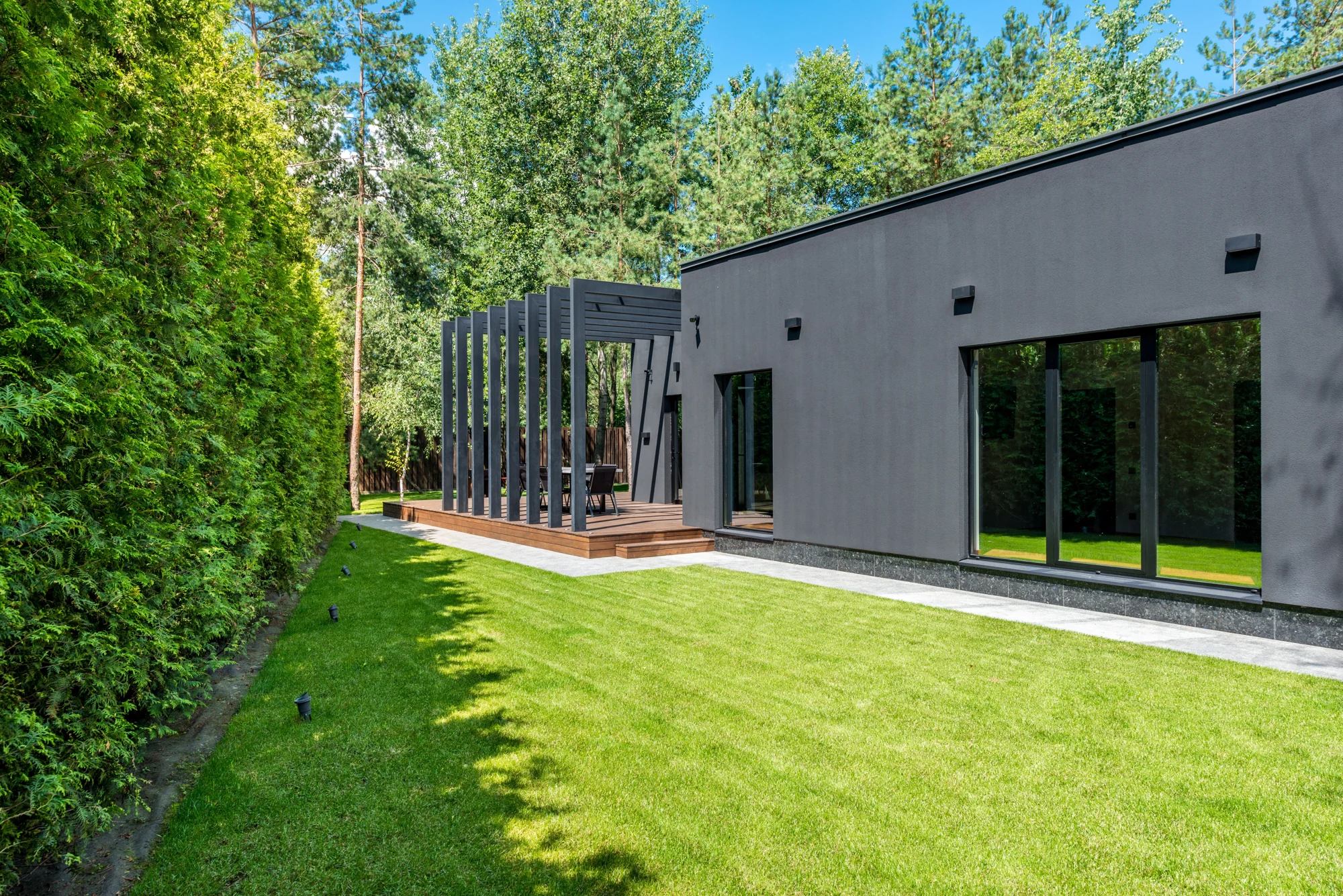 Modernes Einfamilienhaus mit grossen Fenstern, Holzterrasse und grünem Garten; Inspirationsbild